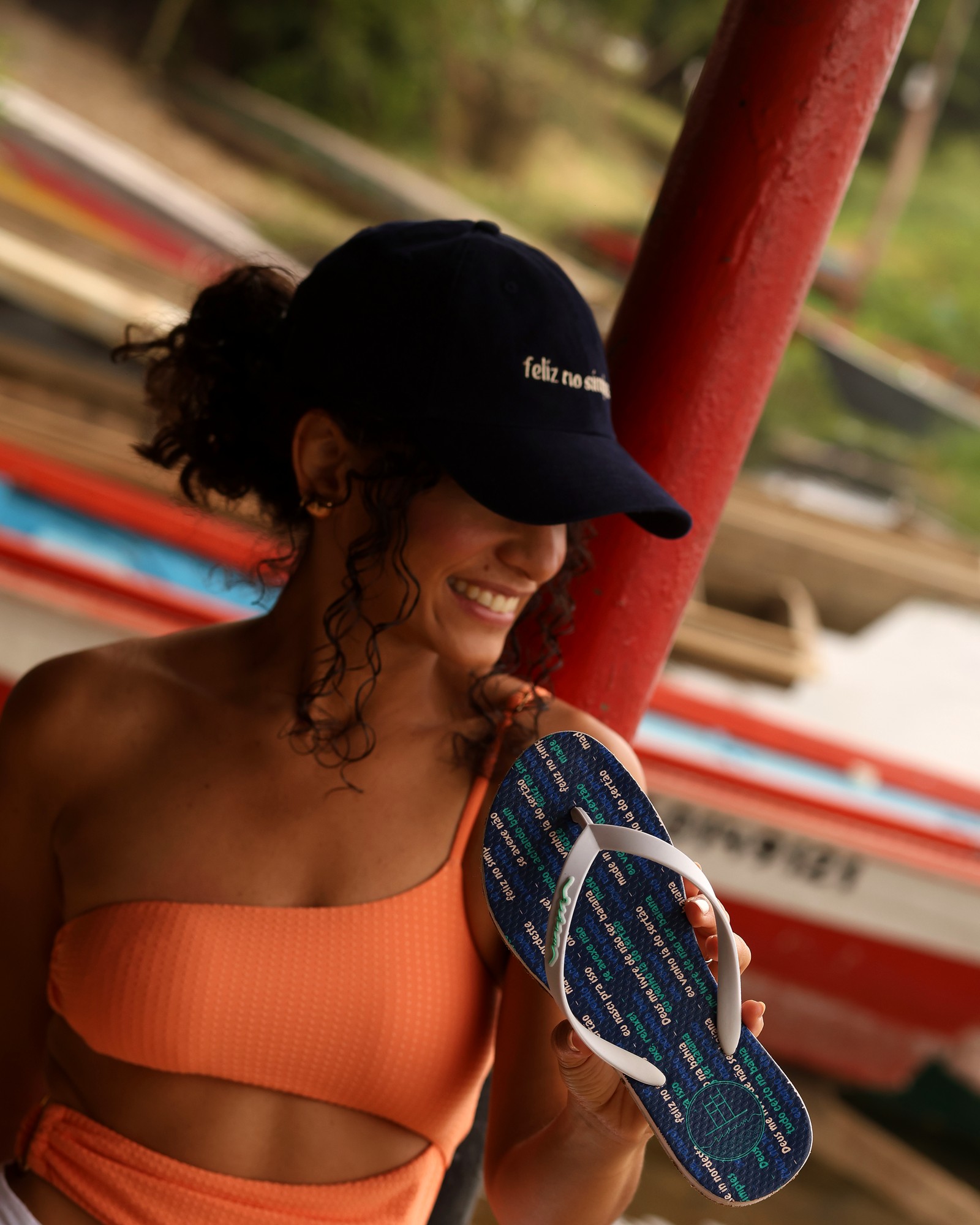 Cliente real da Rivum sorrindo, segurando um boné e um chinelo da marca